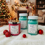 Load image into Gallery viewer, Three hand-poured holiday candles from Southern Charm Farmhouse in mason jar styles, displayed on a white faux fur surface with red Christmas ornaments. The background shows a cozy, blurred living room with a decorated Christmas tree and fireplace.
