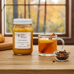 Load image into Gallery viewer, 16 oz mason Jar of 'Fall Festival' hand poured candle, glass mug with hot drink and cinnamon stick, and small bowl of spices on a wooden surface with autumn scenery.  Southern Charm Farmhouse.
