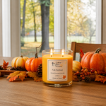 Load image into Gallery viewer, A lit two-wick Fall Festival scented candle in a clear glass jar sits on a wooden table surrounded by pumpkins, fall leaves, pinecones, and berries, with a window and blurred outdoor scenery in the background. Southern Charm Farmhouse.
