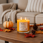 Load image into Gallery viewer, A lit double-wick candle in a clear glass jar sits on a wooden table in a cozy living room setting. The candle label reads 'Fall Festival Candle 16 oz Made in Texas. Southern Charm Farmhouse.
