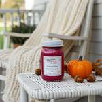 Load image into Gallery viewer, 16 oz mason Jar of 'Fireside Glow' hand poured candle on a white surface with pumpkins and acorns, outdoor setting.  Southern Charm Farmhouse.
