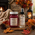 Load image into Gallery viewer, Two Southern Charm Farmhouse scented products displayed on a rustic wooden surface: a jar candle labeled 'Fireside Glow' with deep red wax and a clear room spray bottle labeled 'Cedar &amp; Autumn Leaves' with amber liquid. The scene is styled with fall decor including autumn leaves, pinecones, a pumpkin, a lantern, a cozy knit blanket, and a fireplace in the background.
