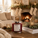 Load image into Gallery viewer, A hand-poured candle in a clear glass jar with a silver lid sits on a wooden table in a cozy living room setting with a lit fireplace, stockings, pinecones, and books. Southern Charm Farmhouse.
