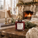 Load image into Gallery viewer, A red holiday scented candle in a clear glass jar with a silver lid sits on a rustic wooden table in a cozy living room with a fireplace, stockings, and books. Southern Charm Farmhouse.
