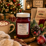 Load image into Gallery viewer, A 16 oz mason jar candle labeled 'Fireside Magic' by Southern Charm Farmhouse is styled on a wooden board in a cozy holiday setting with a mug of marshmallow coffee, pinecones, a red ornament, and a Christmas tree in the background.
