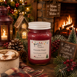 Load image into Gallery viewer, A 16 oz mason jar candle labeled 'Fireside Magic' by Southern Charm Farmhouse. sits on a rustic wooden table surrounded by holiday decorations, including a burning fireplace in the background, a lantern with a lit candle, pinecones, berries, and small Christmas trees.

