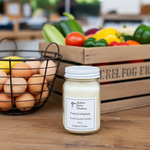 Load image into Gallery viewer, French Market Candle in a 16 oz Mason jar on a wooden surface with eggs and vegetables in the background. Southern Charm Farmhouse.
