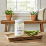 Load image into Gallery viewer, Green Clover &amp; Aloe Candle in a 16 oz Mason jar on a wooden tray on a bench with plants and sunshine behind it. Southern Charm Farmhouse.
