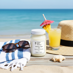 Load image into Gallery viewer, 16 oz Mason jar Hawaiian Tropic candle with straw hat, sunglasses, pineapple drink beside it and ocean behind it. Hand poured candle. Southern Charm Farmhouse.
