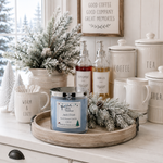 Load image into Gallery viewer, A hand-poured scented candle in a blue glass jar sits on a round wooden tray, styled in a cozy holiday kitchen scene with frosted greenery, ceramic canisters, and a sign that reads 'Good Coffee Good Company Great Memories'. Candle label reads Jack Frost. Southern Charm Farmhouse
