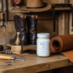 Load image into Gallery viewer, Leather Candle in a 16 oz Mason Jar on a wooden table with leather tools, cowboy hat and cowboy boots in the background. Southern Charm Farmhouse.
