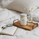Load image into Gallery viewer, Sunwashed Linen hand poured 16 oz Mason jar Candle on a wooden tray with an open book and glasses on a bed and flowers. Southern Charm Farmhouse.
