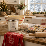 Load image into Gallery viewer, A holiday-themed kitchen scene featuring a jar candle labeled 'Marshmallow Wonderland' on a wooden countertop, surrounded by baking props like a mixing bowl, cookies on a cooling rack, a red towel, and a rolling pin. The background shows a cozy kitchen with winter scenery outside the window. Southern Charm Farmhouse.
