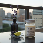 Load image into Gallery viewer, 16 oz Hand Poured Candle labeled 'Midsummer's Night' with a bottle of lavender and a lime wedge on a reflective surface with a cityscape background. Southern Charm Farmhouse.
