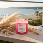 Load image into Gallery viewer, Pink 2 wick hand poured Pink Sands candle on a ledge overlooking a beach. Southern Charm Farmhouse.
