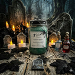 Load image into Gallery viewer, A Halloween-themed hand poured candle display featuring a 16 oz mason  jar candle labeled 'Poison Apple' by Southern Charm Farmhouse, surrounded by smaller bottles and candles on a rustic wooden surface with tombstones, skulls, and black leaves.
