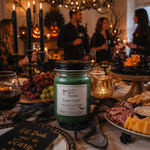 Load image into Gallery viewer, A green hand-poured candle in a 16 oz mason jar with a black lid and a white label reading 'Poison Apple' by Southern Charm Farmhouse., set on a Halloween-themed table with candles, grapes, charcuterie, and blurred people in the background.
