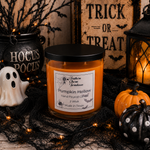 Load image into Gallery viewer, A Halloween-themed candle in a clear glass jar with a silver lid and a white label reading 'Pumpkin Hollow' by Southern Charm Farmhouse. The candle is styled on a rustic surface with black spiderweb, a small white ghost, black cauldron decor, a lantern, pumpkins, and a sign that says 'Trick or Treat'.
