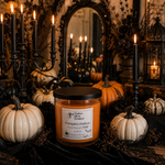 Load image into Gallery viewer, A hand-poured candle in a clear glass jar with a black lid, labeled 'Pumpkin Hollow' by Southern Charm Farmhouse, styled on a table with pumpkins, black candles, and a mirror in a dark, cozy autumn setting.
