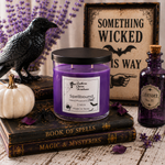 Load image into Gallery viewer, A purple wax hand poured candle labeled Spellbound in a clear glass jar with a black lid sits on stacked vintage-style books, surrounded by Halloween props including a black raven figurine, a small white pumpkin, purple flowers, a purple apothecary bottle labeled Lavender No. 30, and a framed sign reading 'Something Wicked This Way. Southern Charm Farmhouse.
