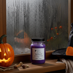 Load image into Gallery viewer, Purple hand poured candle labeled 'Spellbound' on a windowsill with Halloween decorations. Southern Charm Farmhouse.
