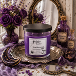 Load image into Gallery viewer, Purple wax candle in a glass jar with a black lid, labeled 'Spellbound' by Southern Charm Farmhouse, styled on a silver tray with purple roses, a mirror, and potion bottles.
