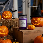 Load image into Gallery viewer, Purple hand poured candle labeled 'Spellbound' surrounded by carved pumpkins and Halloween decorations. Southern Charm Farmhouse.
