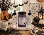 Load image into Gallery viewer, One Spellbound hand poured candle and one room spray and linen spray from Southern Charm Farmhouse are displayed on a rustic white tray. The set includes a purple jar candle and two clear spray bottles with black caps, styled with Halloween props like a mug reading 'WITCHES BREW', black pumpkins, a lantern, and cookies on a table runner.
