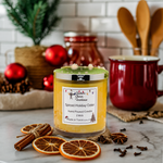 Load image into Gallery viewer, A hand-poured candle labeled 'Spiced Holiday Cider' sits on a marble surface with dried orange slices, cinnamon sticks, star anise, and red ornaments in a warm holiday kitchen setting. Southern Charm Farmhouse 
