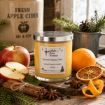 Load image into Gallery viewer, A hand-poured Spiced Holiday Cider candle in a clear glass jar with a silver lid sits on a rustic wooden surface surrounded by spiced cider ingredients, including cinnamon sticks, star anise, dried orange slices, a whole orange, a sliced apple, and a dried orange peel. In the background, a burlap sack labeled 'Fresh Apple Cider' and potted greenery are visible. Southern Charm Farmhouse 
