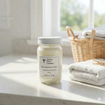 Load image into Gallery viewer, Hand poured Candle jar labeled 'Sunwashed Linen' on a surface with a basket of towels in the background. Southern Charm Farmhouse.
