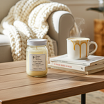 Load image into Gallery viewer, 16 oz Mason Jar of Sweet Vanilla Caramel hand poured candle and steaming mug on a wooden table with books, cozy blanket in background. Southern Charm Farmhouse
