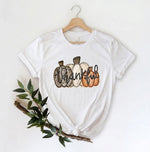 Load image into Gallery viewer, White t-shirt with 'Thankful' pumpkins graphic on a hanger with a branch and leaves. Southern Charm Farmhouse.
