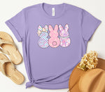 Load image into Gallery viewer, A purple t-shirt with a graphic design of three stylized bunnies wearing floral patterns. Southern Charm Farmhouse.
