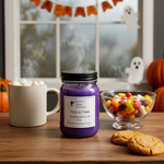 Load image into Gallery viewer, Purple hand poured candle labeled 'Trick or Treat' on a table with Halloween decorations including pumpkins, candy, and ghost figures. Southern Charm Farmhouse.
