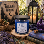 Load image into Gallery viewer, A blue hand-poured candle in a clear glass jar with a black lid sits on a wood slice in a styled tabletop scene. The label reads 'Twilight Woods' and 'Southern Charm Farmhouse.
