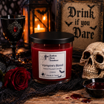 Load image into Gallery viewer, A Halloween-themed product photo of a Southern Charm Farmhouse 'Vampire's Blood' scented candle. The candle is in a clear glass jar with red wax and a black lid, styled on a rustic wooden table with a red rose, a skull, a goblet, and a gothic sign in the background.
