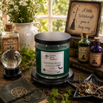 Load image into Gallery viewer, A green glass candle jar labeled 'Witches Brew' sits on a black base in a styled tabletop scene with witch-themed props including a crystal ball, potion bottles, a spellbook, herbs, and a framed sign. Southern Charm Farmhouse.
