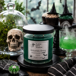 Load image into Gallery viewer, A hand-poured candle in a clear glass jar with a black lid sits on a black tray in a styled Halloween scene. The candle label reads 'Southern Charm Farmhouse' and 'Witches Brew'.
