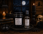 Load image into Gallery viewer, Two gothic-themed candles from Southern Charm Farmhouse, including a large black jar candle labeled 'Black Magic' and a smaller clear spray bottle labeled 'Black Magic Spell Scaler', displayed on a dark tray with Halloween props like a cauldron, skull, spider, and candles. 
