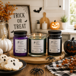 Load image into Gallery viewer, Three Halloween-themed hand-poured candles in glass jars with black lids are displayed on a wooden board in a kitchen setting. The candles are labeled 'Spelkbond' in purple wax, 'Witch's Brew' in green wax and lit, and 'Black Magic' in black wax. Southern Charm Farmhouse
