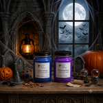 Load image into Gallery viewer, Two hand-poured candles in glass jars, one blue and one purple, displayed on a wooden table in a spooky Halloween-themed setting with a full moon, bats, a pumpkin, and tombstones. Southern Charm Farmhouse
