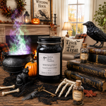 Load image into Gallery viewer, A Halloween-themed tabletop scene featuring a black hand poured candle jar labeled 'Witching Hour' by Southern Charm Farmhouse, surrounded by a cauldron with colorful smoke, books, bones, a skull, and autumn decor in a cozy room setting.
