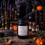 Load image into Gallery viewer, A hand-poured candle Witching Hour in a clear 16 oz mason  jar with a black lid sits on a rustic wooden table surrounded by Halloween-themed props, including candles, books, small bottles, lavender, and jack-o'-lanterns. Southern Charm Farmhouse.
