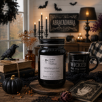 Load image into Gallery viewer, A 16 oz Mason  jar hand poured candle labeled 'Southern Charm Farmhouse Witching Hour' sits on a rustic wooden table surrounded by Halloween decor, including a black mug, old books, a small pumpkin, dried flowers, and a black bird figurine, with a cozy room background featuring candles and a sign reading 'ABRACADABRA'.
