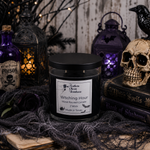 Load image into Gallery viewer, A black jar candle labeled 'Witching Hour' by Southern Charm Farmhouse, styled in a spooky Halloween scene with a skull, books, lanterns, and cobwebs.
