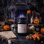 Load image into Gallery viewer, A Halloween-themed hand poured candle display featuring a 16 oz mason jar candle labeled 'Witching Hour' by Southern Charm Farmhouse, surrounded by carved pumpkins, books, cobwebs, a skull, and a black raven in a dark, atmospheric setting.
