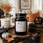 Load image into Gallery viewer, A Halloween-themed hand-poured candle in a clear glass jar with a black lid and white label reading 'Witching Hour' by Southern Charm Farmhouse. The jar sits on a wooden tray in a styled autumn scene with pumpkins, black lace, books, and fall decor.

