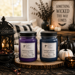 Load image into Gallery viewer, Two hand-poured candles in glass jars, one purple and one dark blue, displayed on a rustic wood slice with Halloween decorations including black lanterns, small pumpkins, and a black sign in the background. Southern Charm Farmhouse
