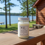 Load image into Gallery viewer, 16 oz Mason Jar of candle labeled 'Lake Side Cabin' on a wooden deck with a lake and cabin in the background. Southern Charm Farmhouse
